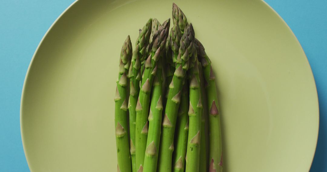 Image of fresh asparagus on green plate over blue background - Free Images, Stock Photos and Pictures on Pikwizard.com