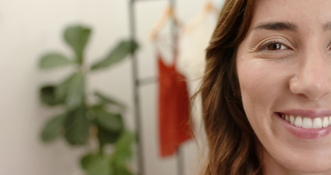 Confident woman smiling in boutique studio with clothing rack, green plant and soft bokeh