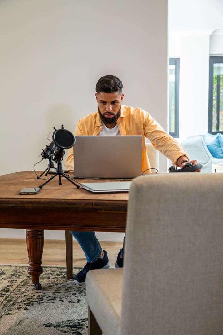 Man Working on Laptop with Microphone in Home Office Setting