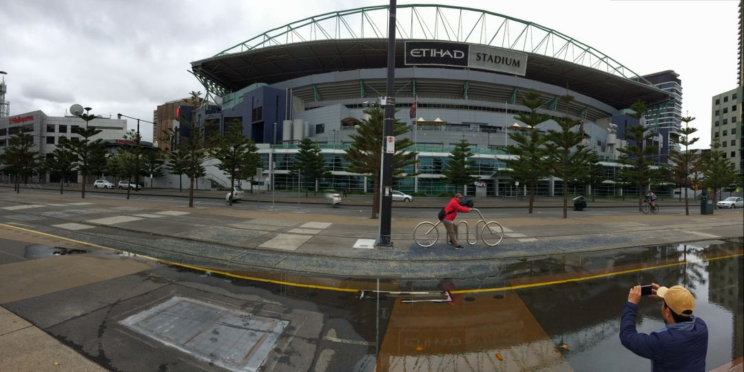 Cyclist passing Etihad Stadium, Melbourne on a cloudy day - Free Images, Stock Photos and Pictures on Pikwizard.com