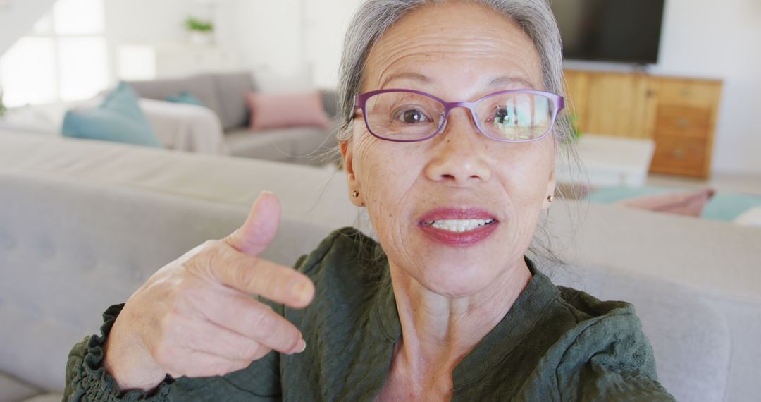 Smiling Elderly Woman Pointing at Camera in Modern Living Room - Free Images, Stock Photos and Pictures on Pikwizard.com