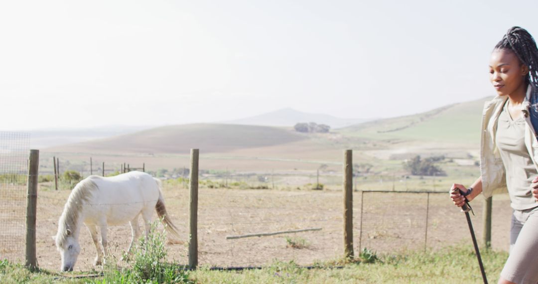 Woman Enjoying Walk Near Grazing Horse on Farm with Scenic Background - Free Images, Stock Photos and Pictures on Pikwizard.com