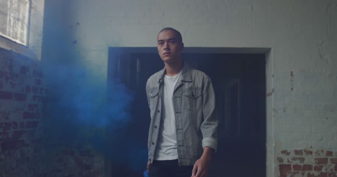 Young Man Standing in Weathered Industrial Room with Blue Smoke - Free Images, Stock Photos and Pictures on Pikwizard.com