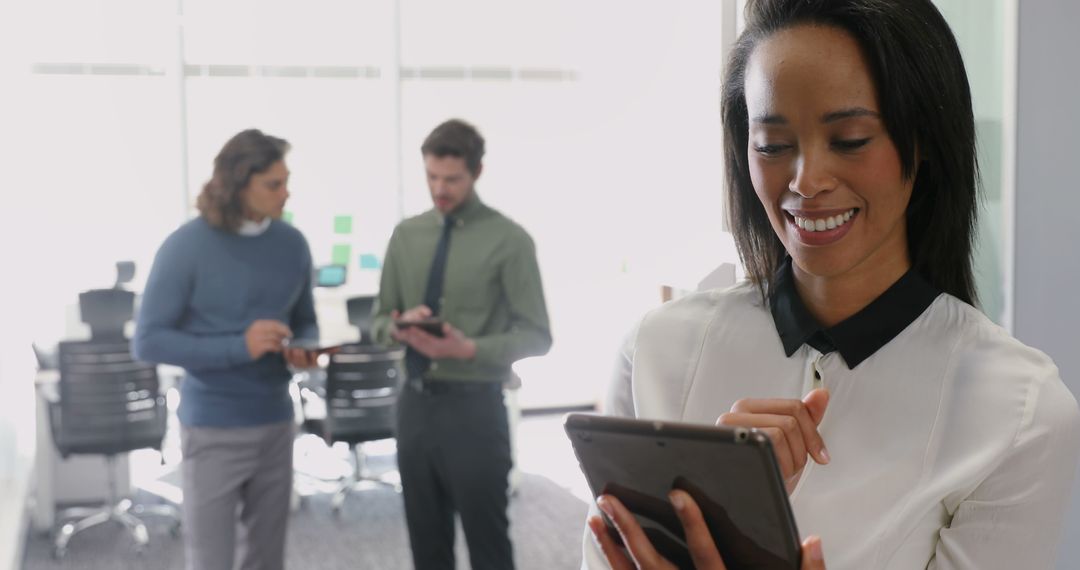 Happy Businesswoman Using Tablet in Office with Colleagues in Background - Free Images, Stock Photos and Pictures on Pikwizard.com