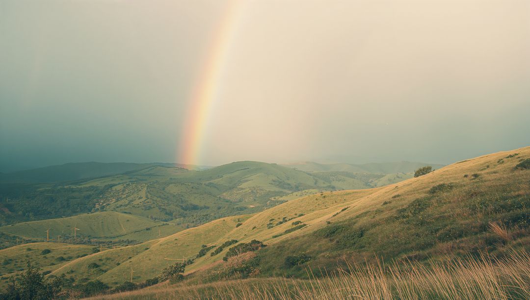 Scenic Rainbow Over Beautiful Grassy Hills with Wind Turbines