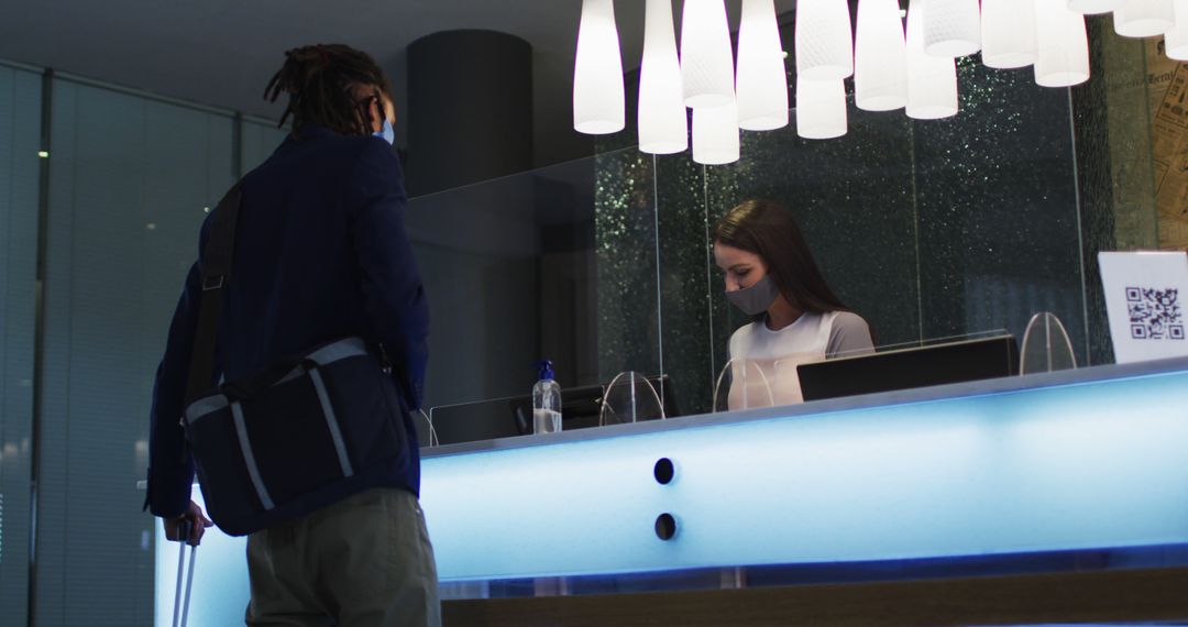 Biracial man and female receptionist wearing face masks at hotel reception desk - Free Images, Stock Photos and Pictures on Pikwizard.com