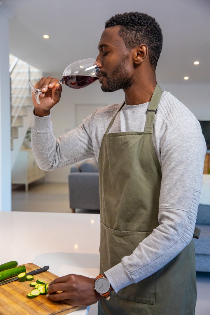 Man Savoring Red Wine While Preparing Meal at Home