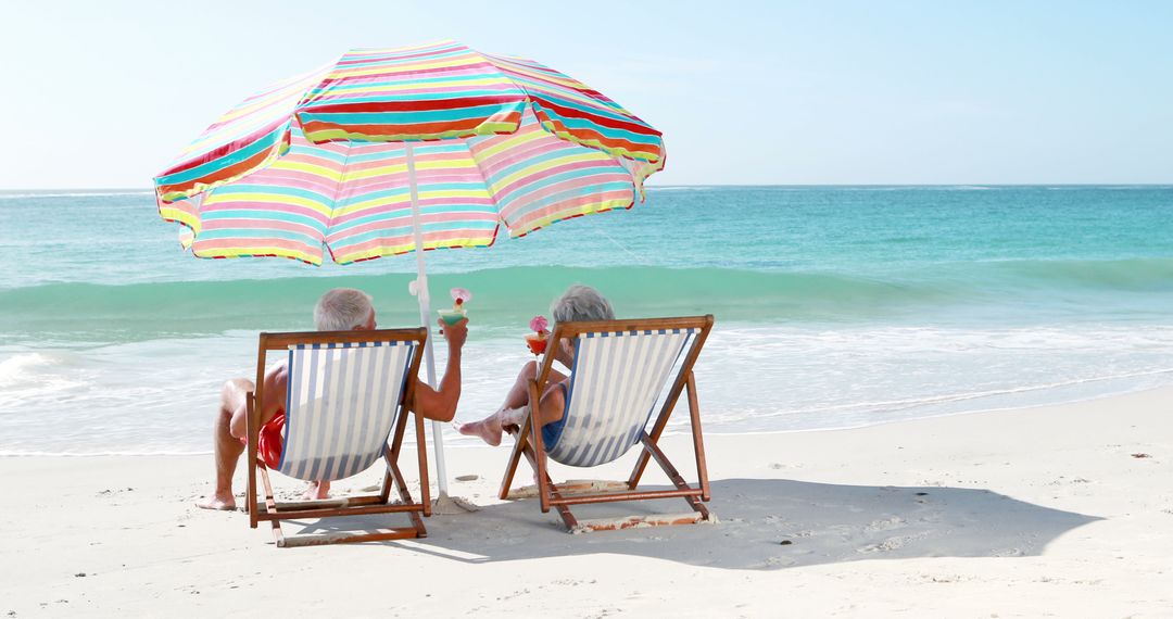 Elderly Couple Relaxing on Tropical Beach with Umbrella and Drinks - Free Images, Stock Photos and Pictures on Pikwizard.com