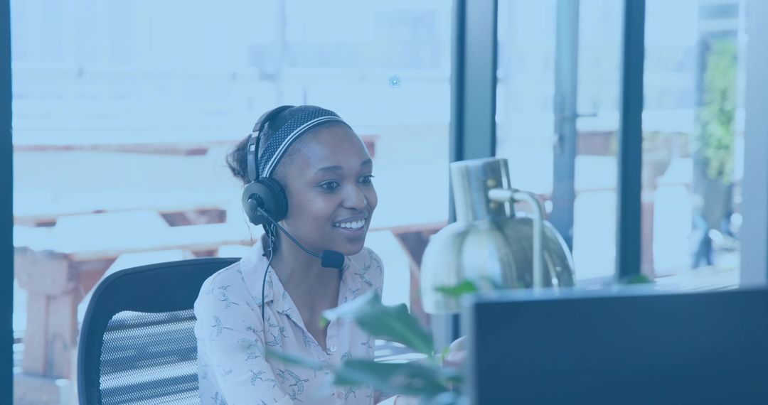 Smiling customer service agent speaking on headset working at bright coworking workstation