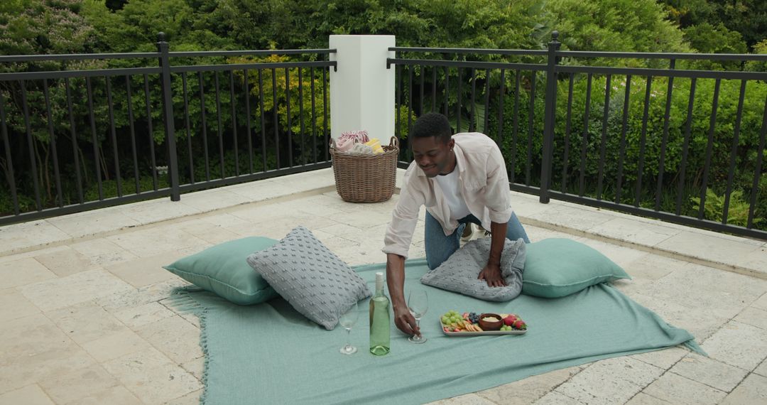 Man Organizing Elegant Picnic on Terrace with Wine and Snacks