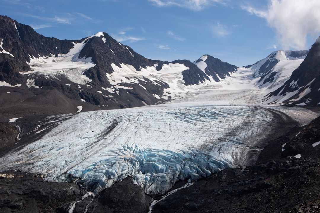 Blue Glacier Flowing Between Rugged Snow-Capped Peaks Under Clear Sky