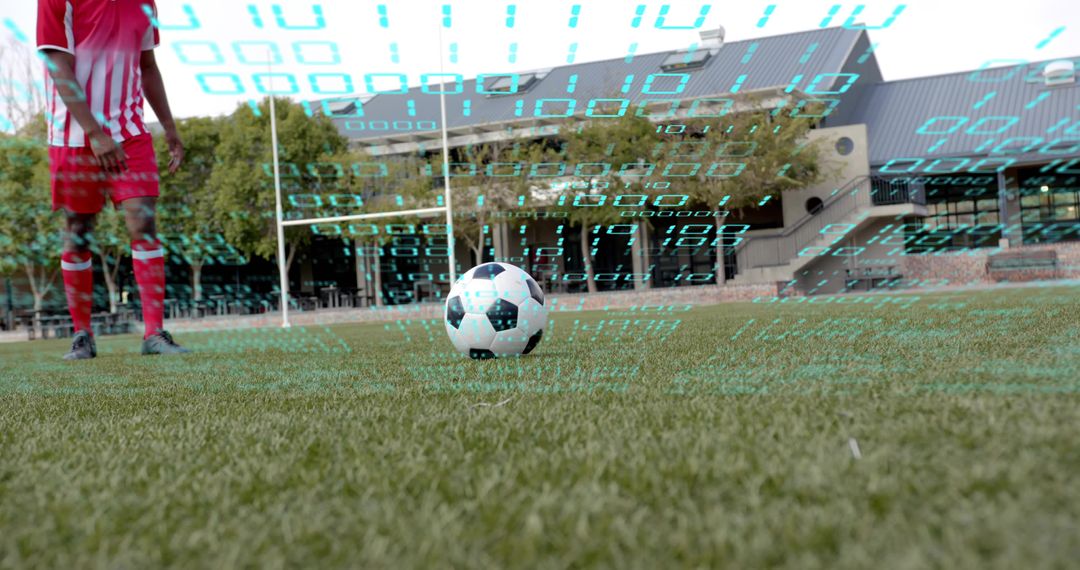 Soccer ball resting on turf with player wearing red-striped kit and digital data overlay