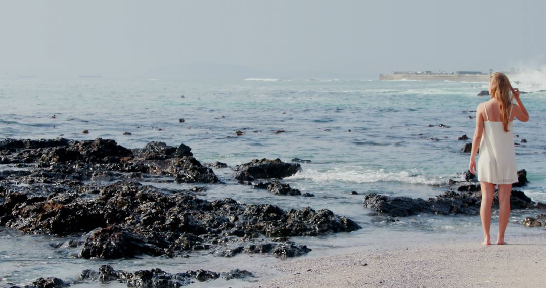 Woman in White Dress Standing on Rocky Seashore with Waves - Free Images, Stock Photos and Pictures on Pikwizard.com