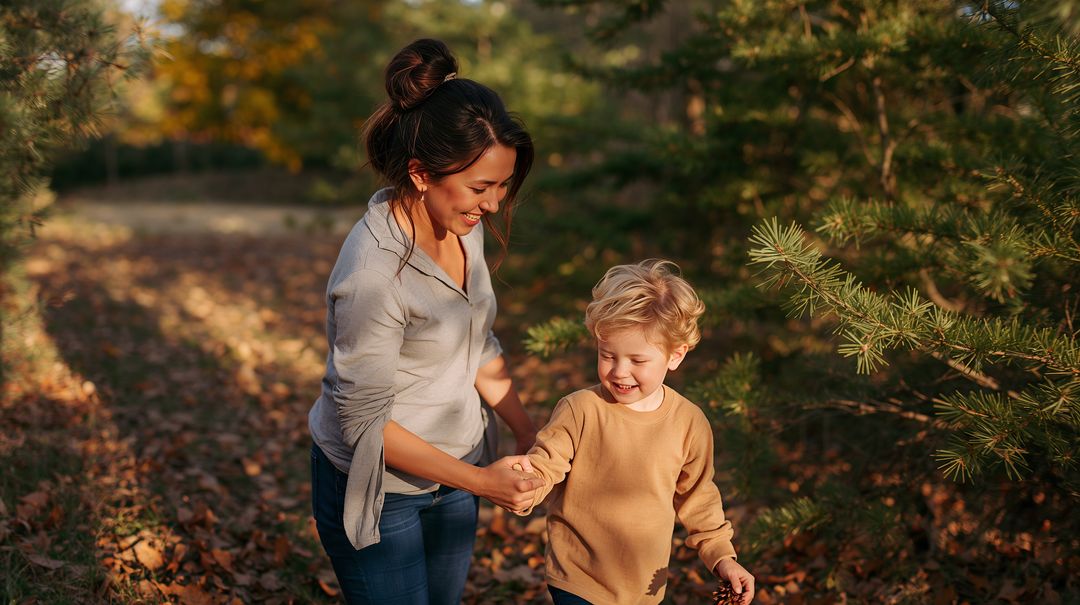 Mother walking with son holding hands on autumn woodland path smiling in golden sunlight