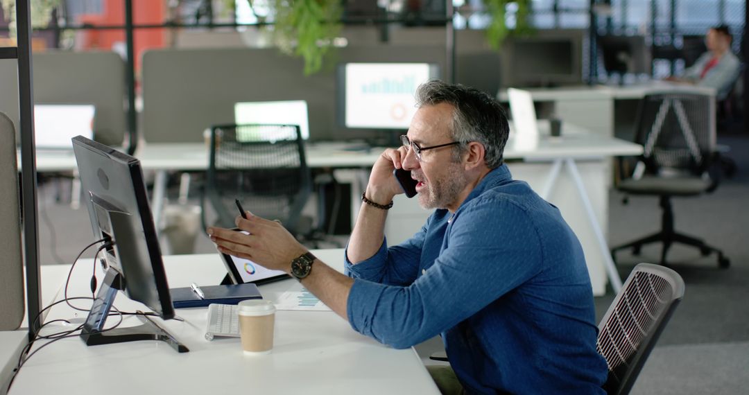 Middle-aged man talking on phone while working at modern office desk
