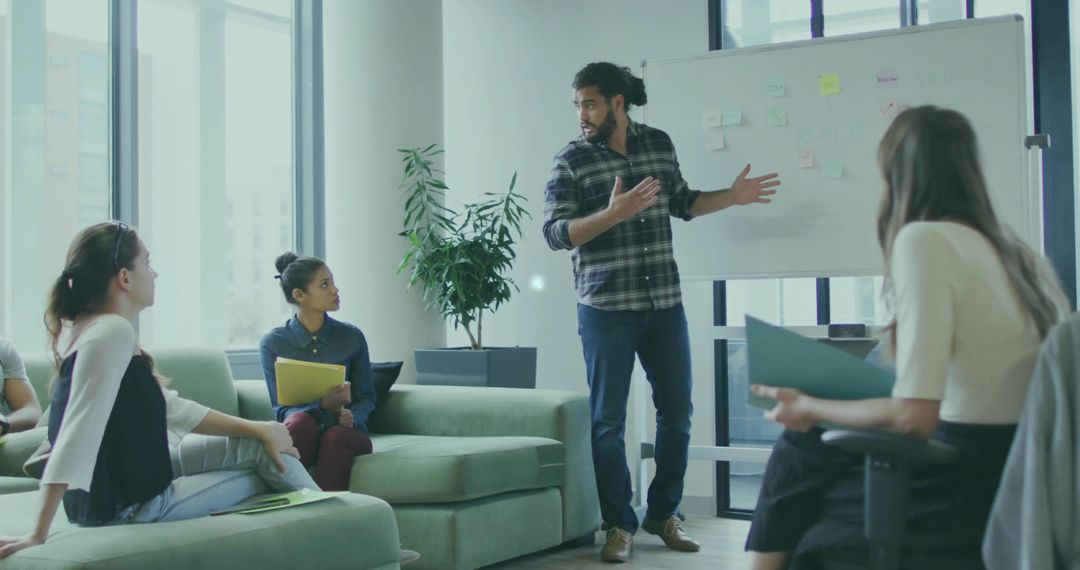 Standing Presenter Gesturing at Whiteboard During Team Brainstorming in Glass Office Space