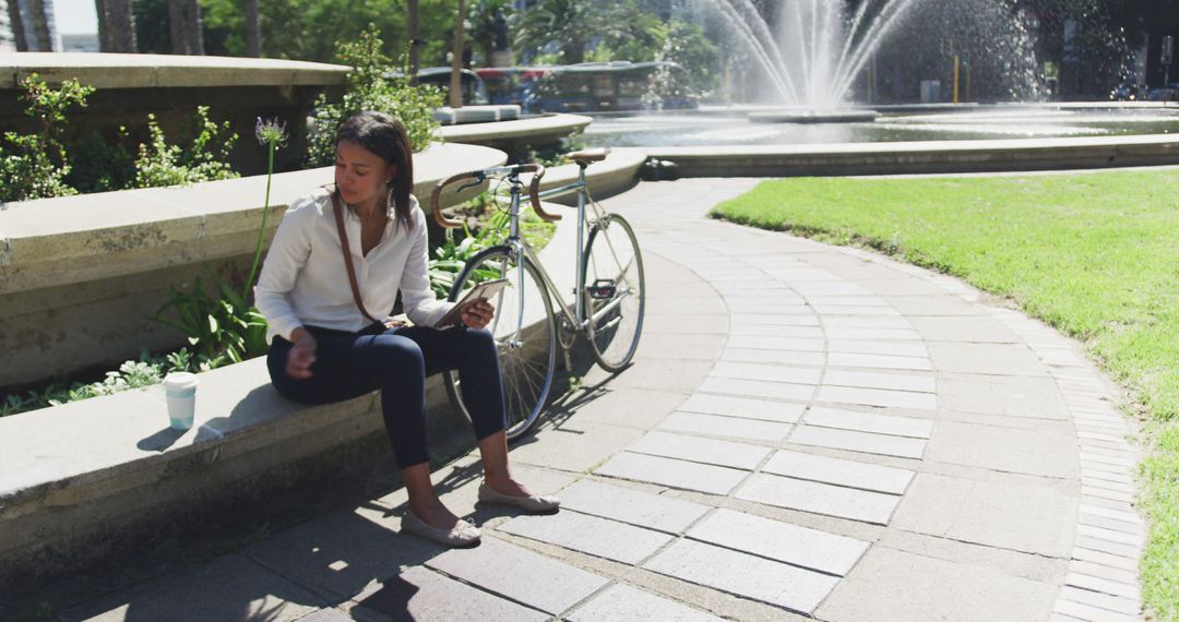 Woman Relaxing in Park with Bicycle and Tablet Near Fountain - Free Images, Stock Photos and Pictures on Pikwizard.com