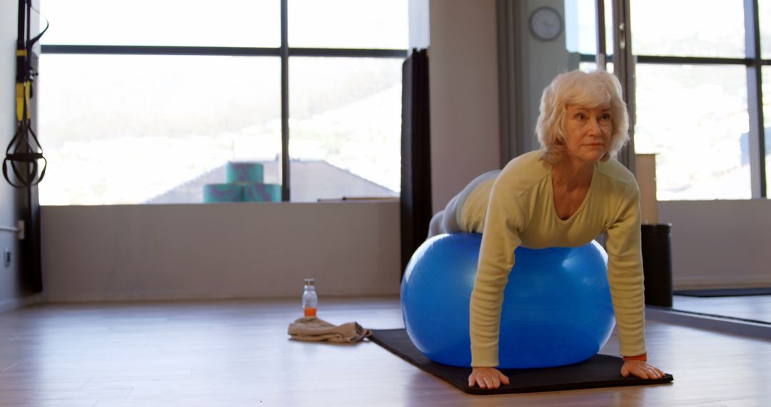 A senior Caucasian woman is exercising on a blue fitness ball in a bright room, with copy space - Free Images, Stock Photos and Pictures on Pikwizard.com