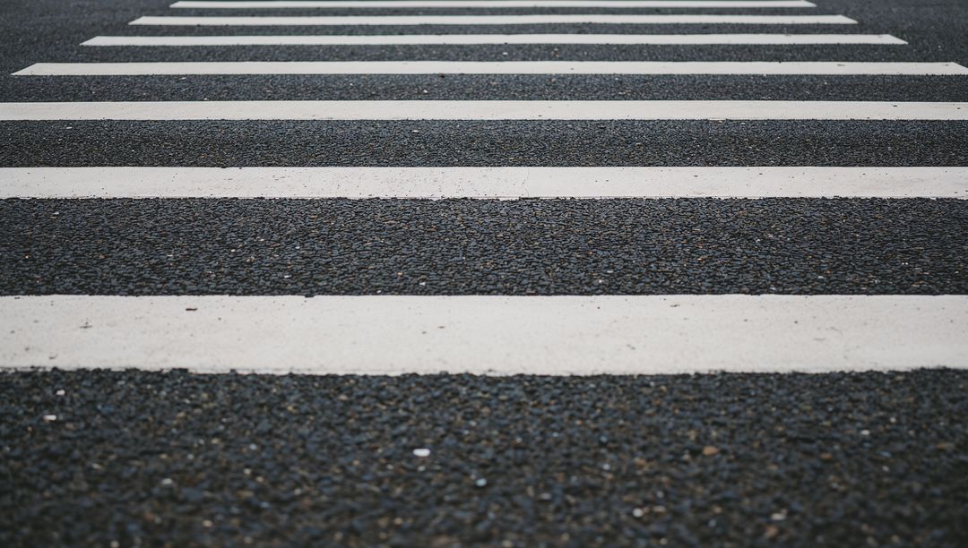 Receding pedestrian crosswalk with bold white stripes on textured asphalt leading lines