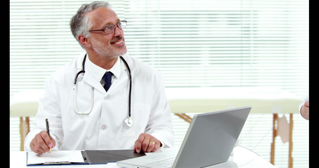 Smiling Senior Doctor Working on Laptop in Medical Office - Free Images, Stock Photos and Pictures on Pikwizard.com