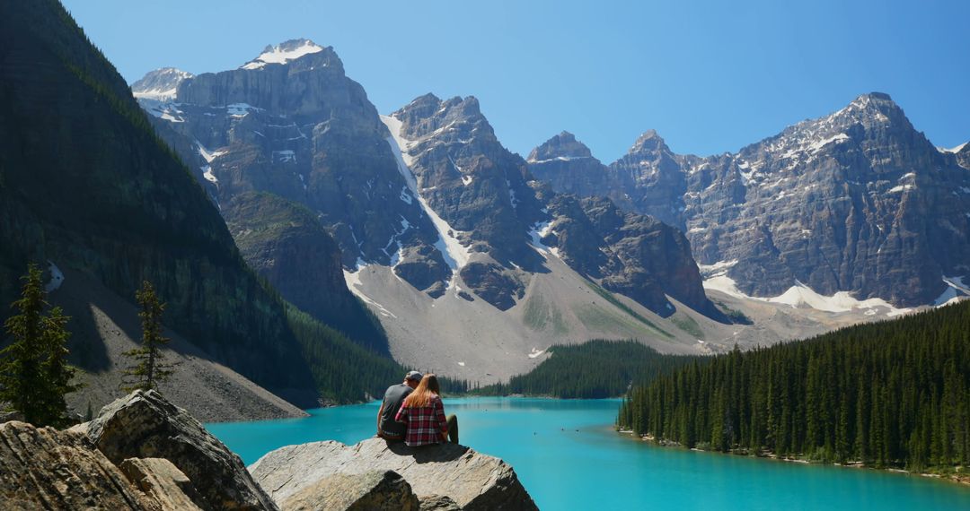 Couple sitting on rock overlooking mountain lake in forest - Free Images, Stock Photos and Pictures on Pikwizard.com