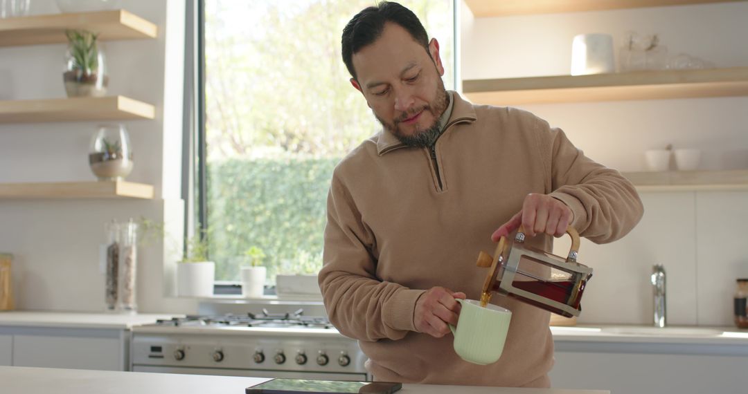 Man Pouring Coffee in Minimalist Kitchen with Natural Light