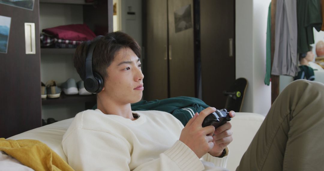 Teen with Headphones Relaxing and Gaming on Couch - Free Images, Stock Photos and Pictures on Pikwizard.com