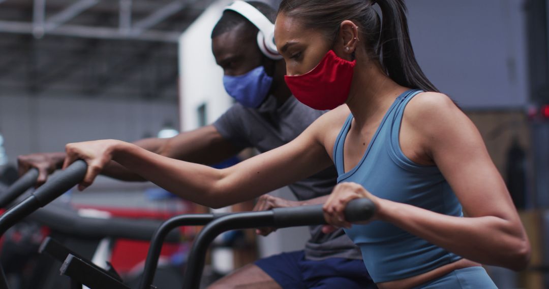 Diverse individuals exercising on stationary bikes wearing face masks in gym - Free Images, Stock Photos and Pictures on Pikwizard.com