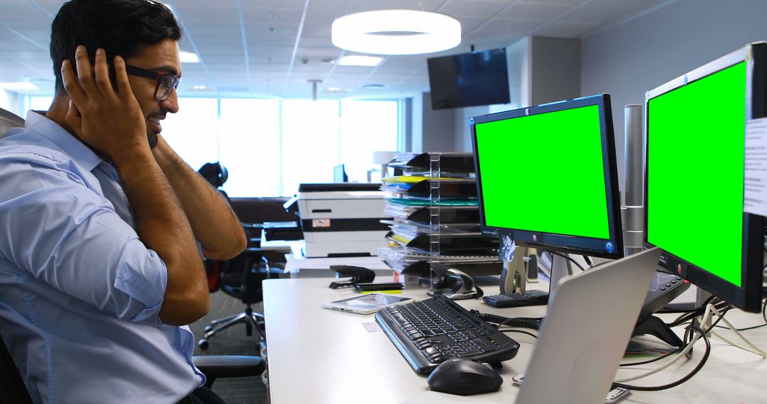 Frustrated Office Worker Covering Ears in Front of Dual Monitors - Free Images, Stock Photos and Pictures on Pikwizard.com