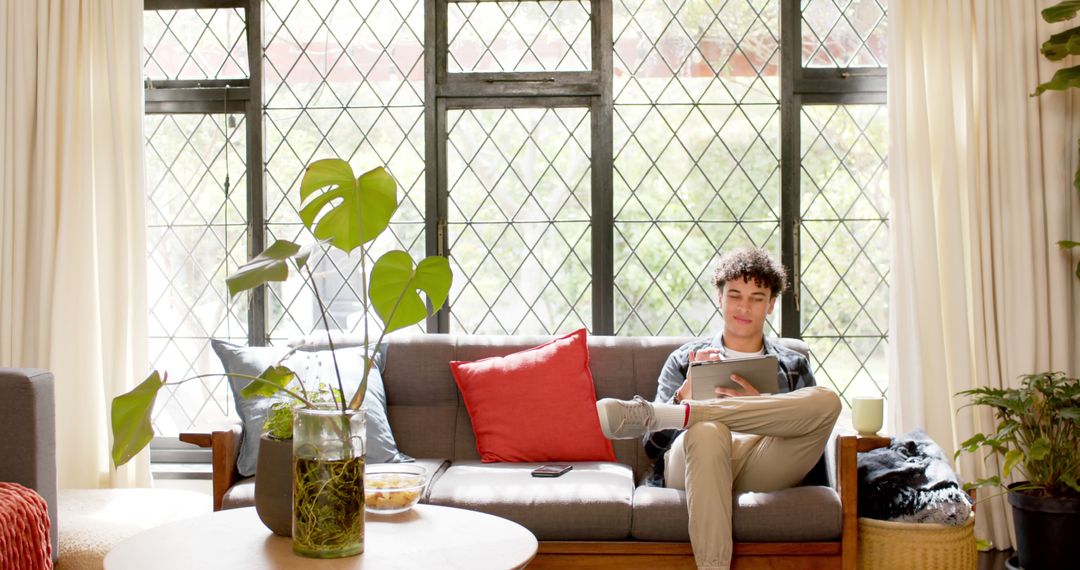 Young Man Relaxing on Couch with Tablet in Bright Living Room - Free Images, Stock Photos and Pictures on Pikwizard.com