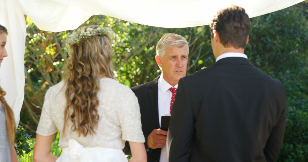 Elegant Outdoor Wedding Ceremony with Bride, Groom, and Officiant Exchanging Vows
