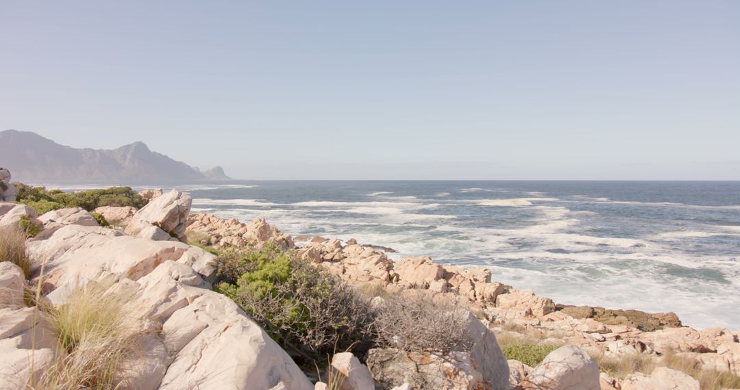 Rocky Coastline with Crashing Waves and Distant Mountains - Free Images, Stock Photos and Pictures on Pikwizard.com