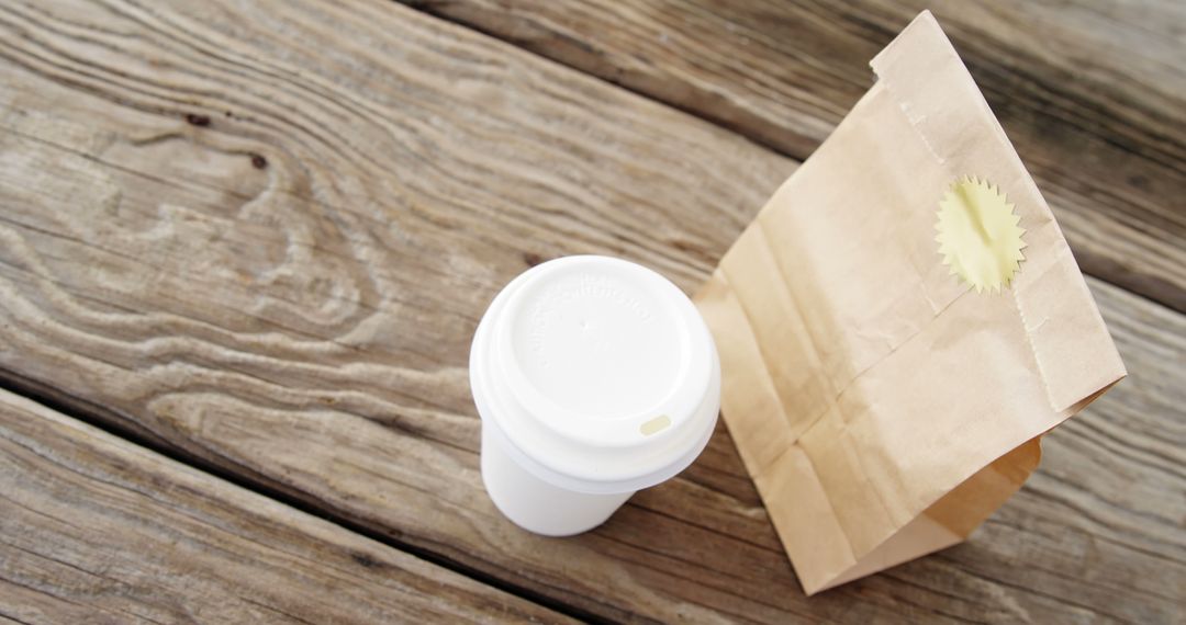 Takeaway coffee cup and brown paper bag on wooden surface - Free Images, Stock Photos and Pictures on Pikwizard.com