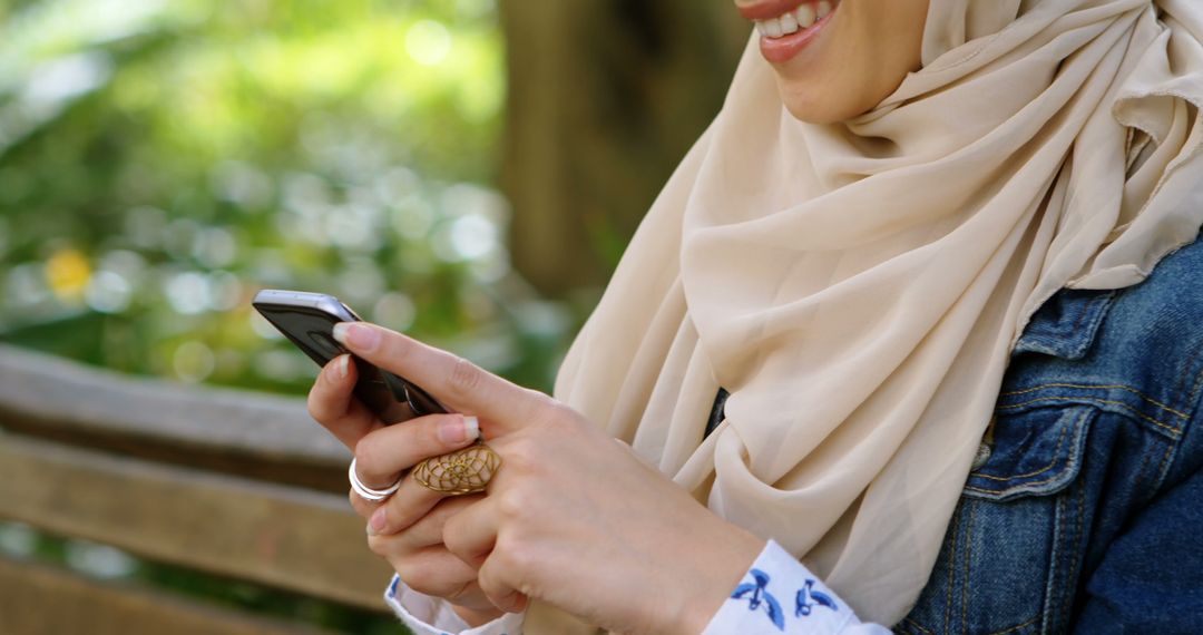 Woman in Hijab Enjoys Texting Outside on Sunny Park Bench - Free Images, Stock Photos and Pictures on Pikwizard.com