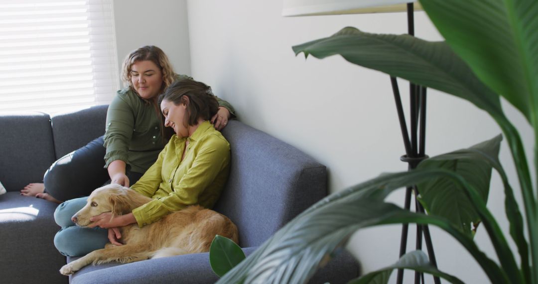 Caucasian lesbian couple smiling and sitting on couch with dog - Free Images, Stock Photos and Pictures on Pikwizard.com