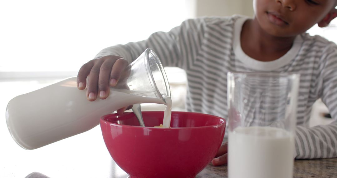 Child Pouring Milk into Red Cereal Bowl at Kitchen Counter - Free Images, Stock Photos and Pictures on Pikwizard.com