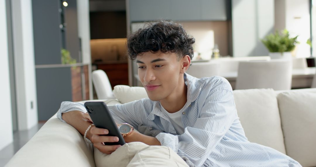 Young Man Relaxing on Modern Sofa Using Smartphone in Stylish Living Room