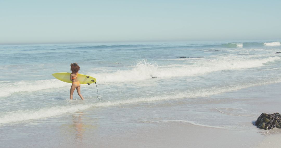 Biracial woman walking on sea and holding surfboard - Free Images, Stock Photos and Pictures on Pikwizard.com