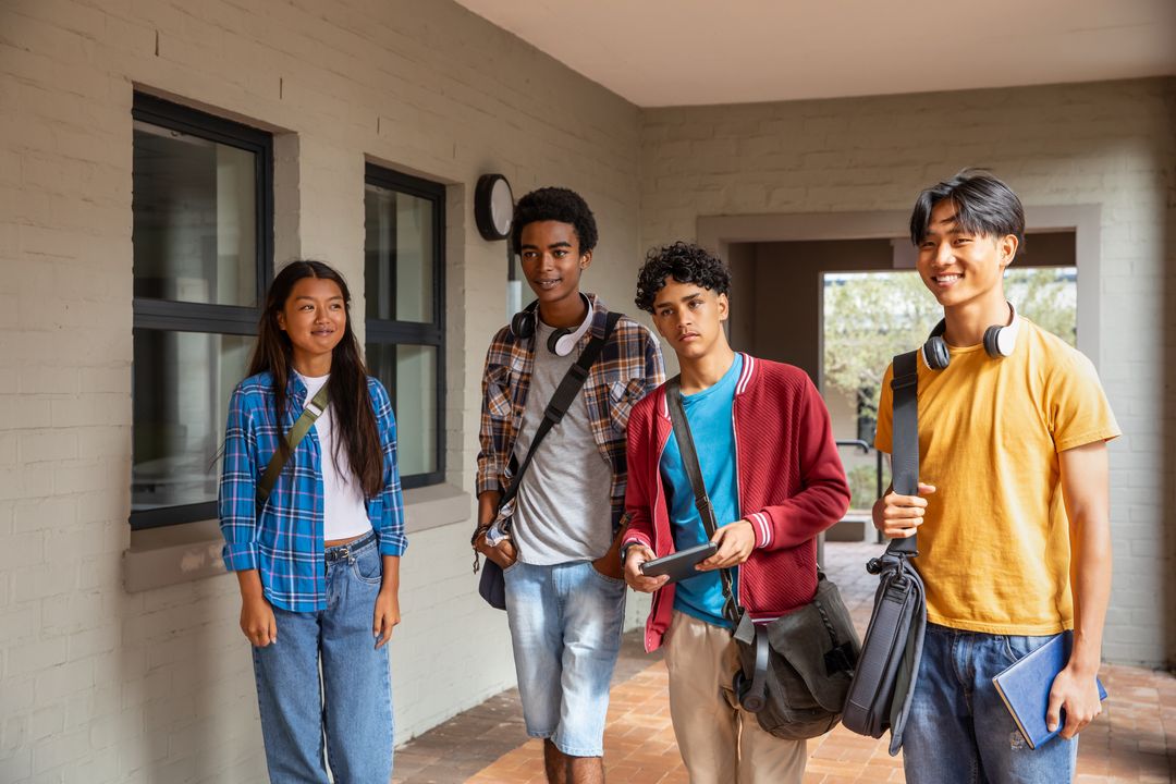 Multicultural students walking and smiling in campus corridor holding tablet and backpacks
