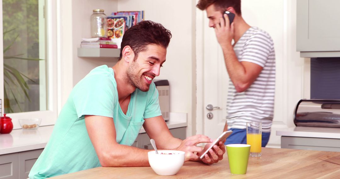 Smiling Man Using Smartphone in Kitchen with Friend on Phone in Background - Free Images, Stock Photos and Pictures on Pikwizard.com