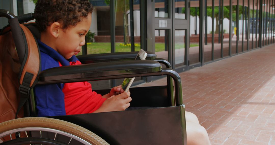 Schoolboy in Wheelchair Using Digital Tablet in Corridor