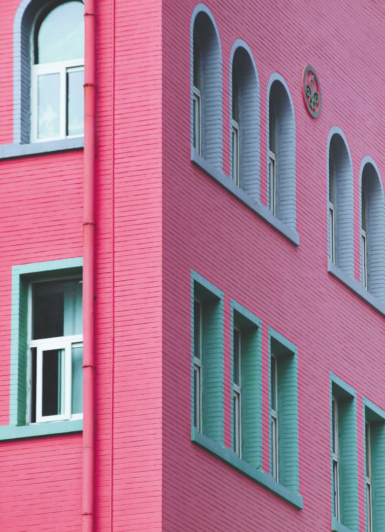 Vibrant Pink Teal Building Facade Featuring Arched Windows and Geometric Lines