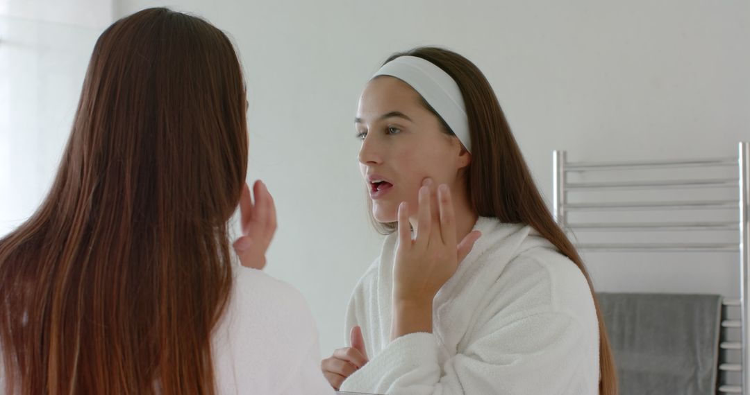 Young Woman in Robe Checking Skin in Mirror for Skincare Routine