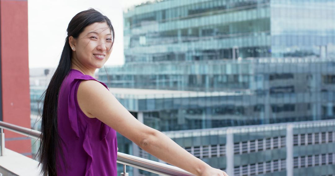 Smiling Woman in Purple Top Standing on Balcony with Urban Background - Free Images, Stock Photos and Pictures on Pikwizard.com