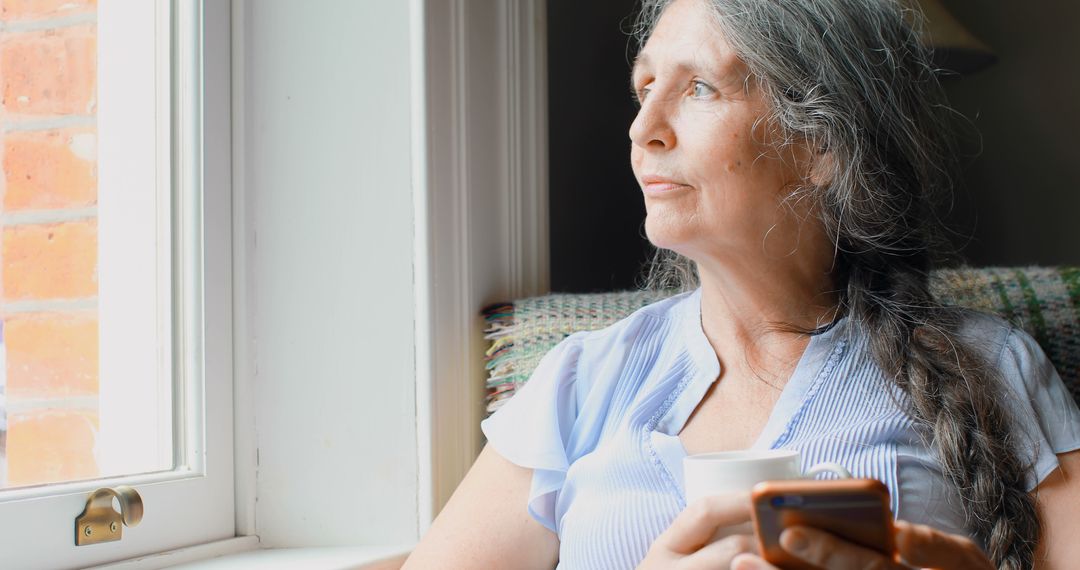 Senior Woman Relaxing with Coffee and Smartphone by Sunny Window - Free Images, Stock Photos and Pictures on Pikwizard.com