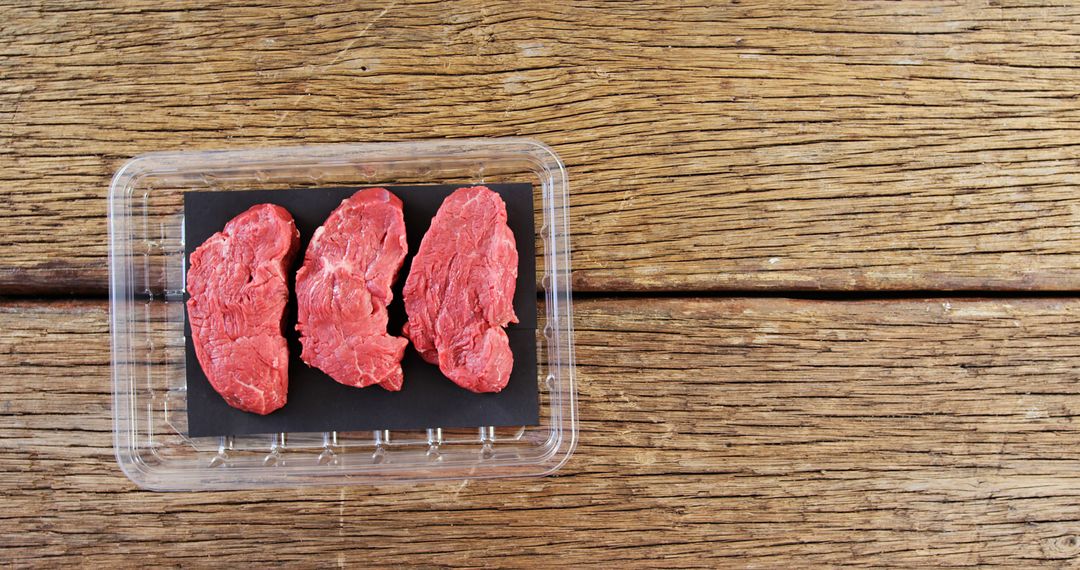 Three Raw Beef Steaks in Plastic Container on Wooden Surface - Free Images, Stock Photos and Pictures on Pikwizard.com