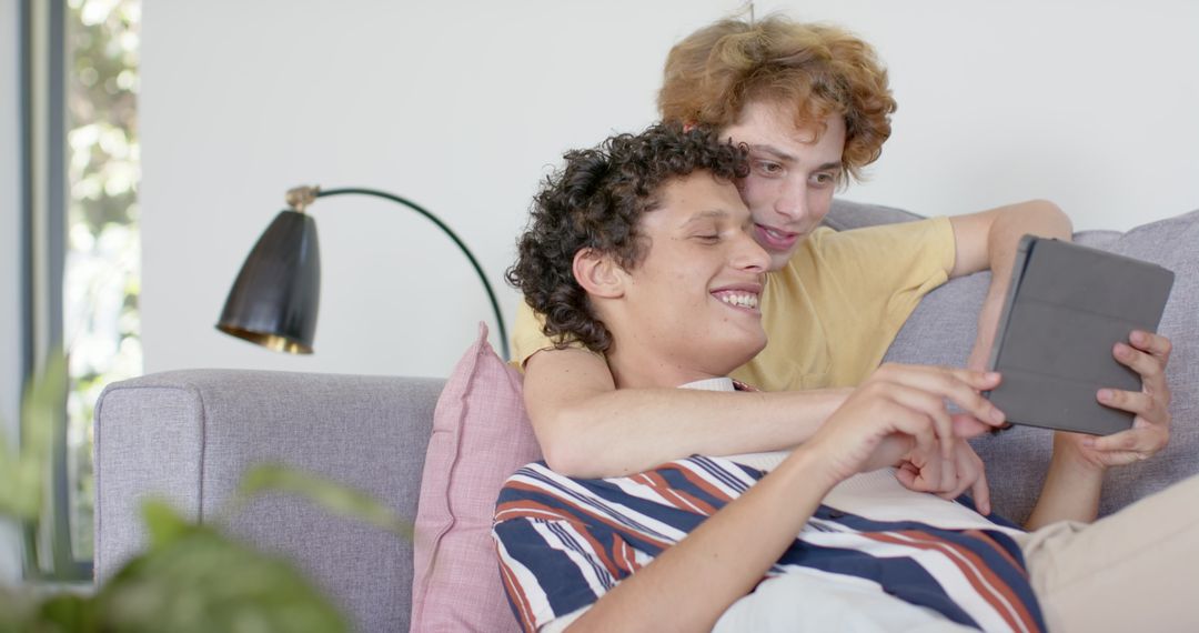 Joyful couple at home using digital tablet on sofa