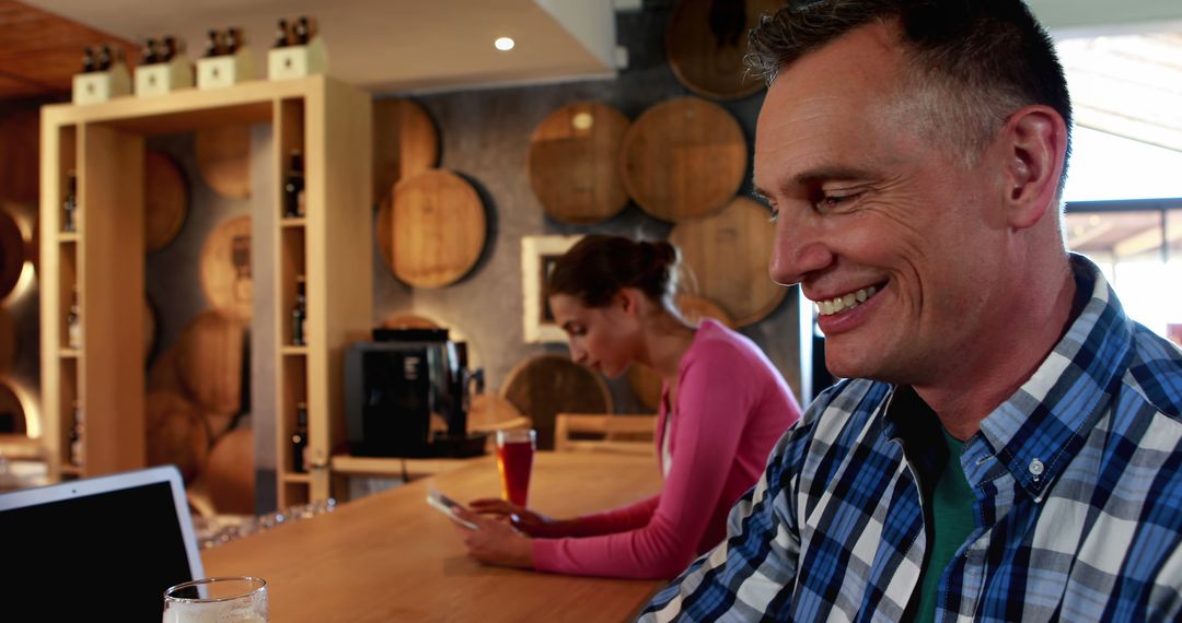 Smiling Man Working on Laptop in Rustic Bar with Wine Barrels