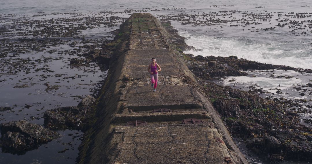 Woman Jogging on Seaside Promenade Amidst Rocky Shoreline - Free Images, Stock Photos and Pictures on Pikwizard.com