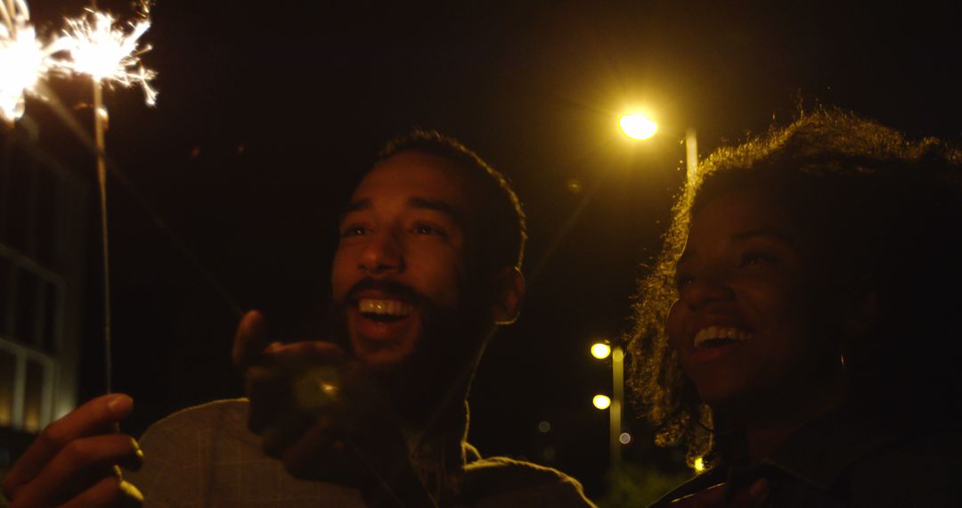 Romantic diverse couple smiling and holding sparklers in city street at night - Free Images, Stock Photos and Pictures on Pikwizard.com